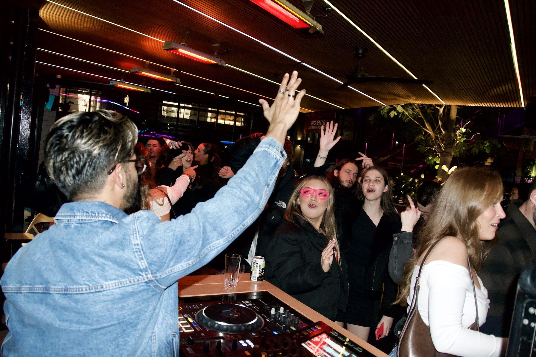 Dr Darp with a hand in the air at the decks as the crowd dances behind him
