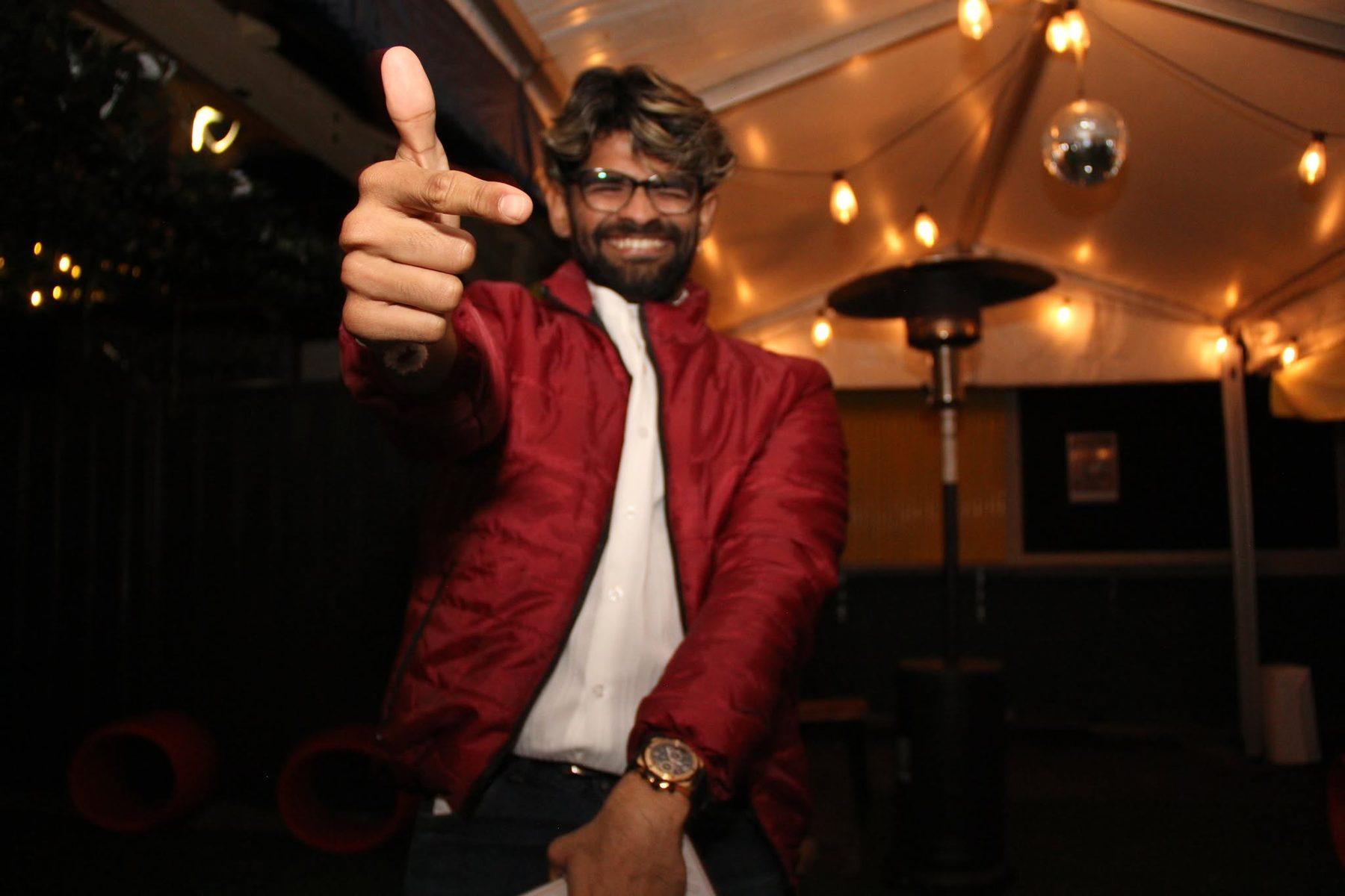Dr Darp in a red jacket pointing at the camera under outdoor fairy lights