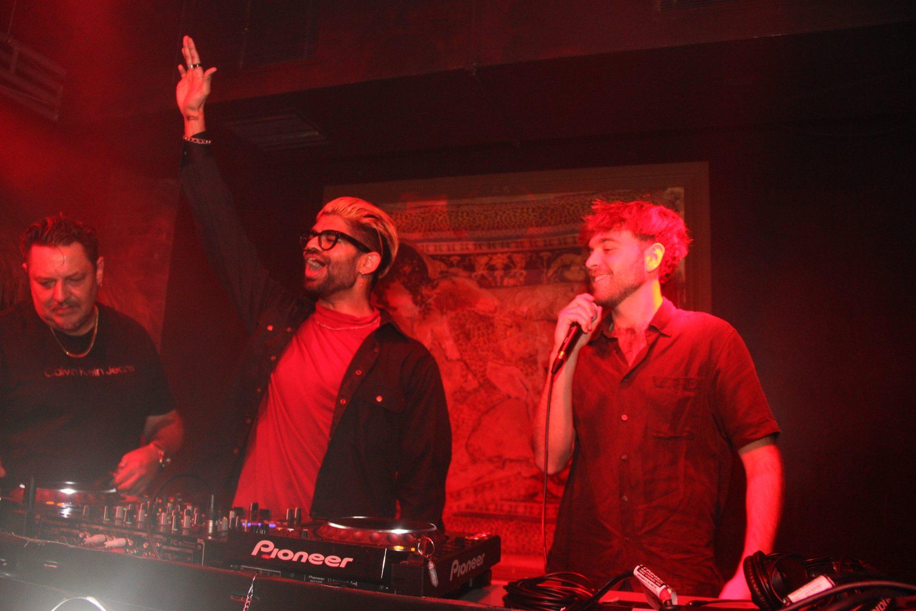 Dr Darp with his hand raised behind the decks under red stage light